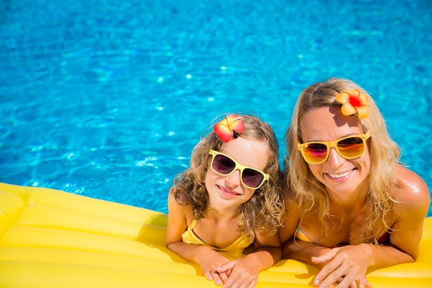 Feliz mãe e filha com óculos de sol e flores no cabelo na piscina
