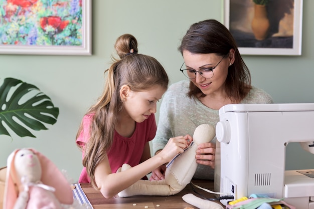 Feliz mãe e filha costurando a boneca coelhinha de brinquedo em casa. família, hobbies e lazer, criatividade, estilo de vida, habilidades e aprendizagem, comunicação entre pais e filhos, dia das mães