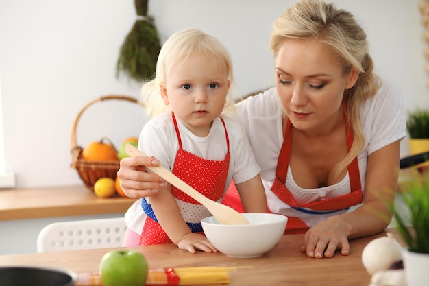 Feliz mãe e filha cozinhando na cozinha. Passar o tempo todos juntos, conceito de diversão em família.