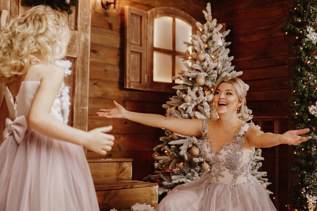 Feliz mãe e filha em vestidos rosa perto das decorações de Natal