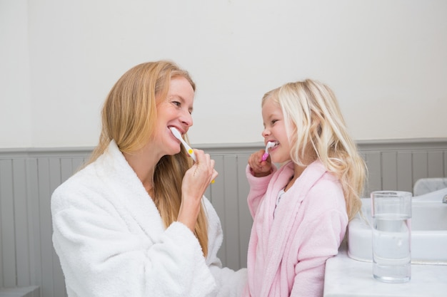 Foto feliz mãe e filha escovando os dentes