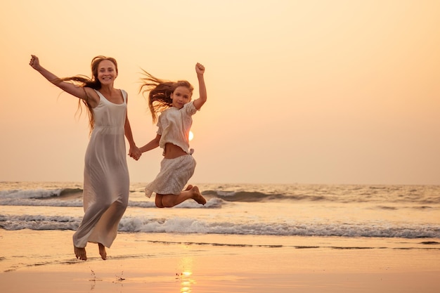 Feliz mãe e filha na praia ao pôr do sol se divertindo à beira-mar. brincando de mulher pulando e regozijando e seu filho copyspace copyspace