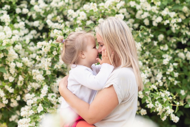 Feliz mãe e filha no parque em um dia ensolarado ao pôr do sol Mãe e filho ao ar livre Conceito de ternura família mãe solteira flores sorrisos abraços harmonia de saúde mental