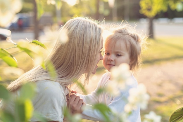 Feliz mãe e filha no parque em um dia ensolarado ao pôr do sol Mãe e filho ao ar livre Conceito de ternura família mãe solteira flores sorrisos abraços saúde mental harmonia férias