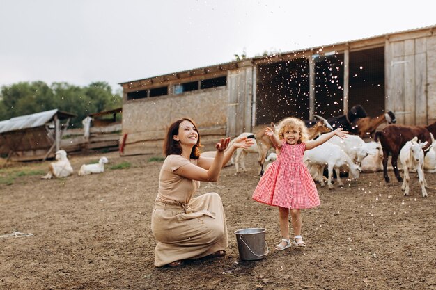 Feliz mãe e filha passam um tempo em uma fazenda ecológica entre cabras.