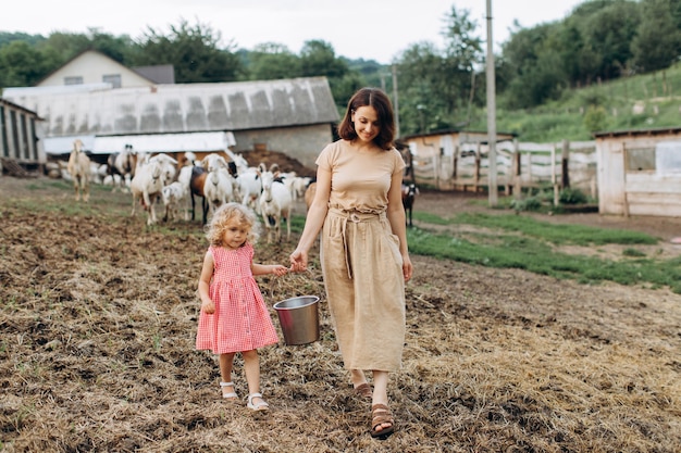 Foto feliz mãe e filha passam um tempo em uma fazenda ecológica entre cabras.