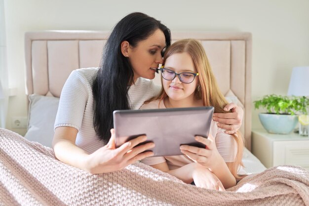 Feliz mãe e filha pré-adolescente abraçando juntos olhando para a tela do tablet digital