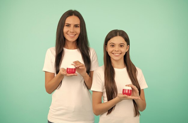 Feliz mãe e filha seguram frasco cosmético com produto de beleza nas mãos creme para a pele