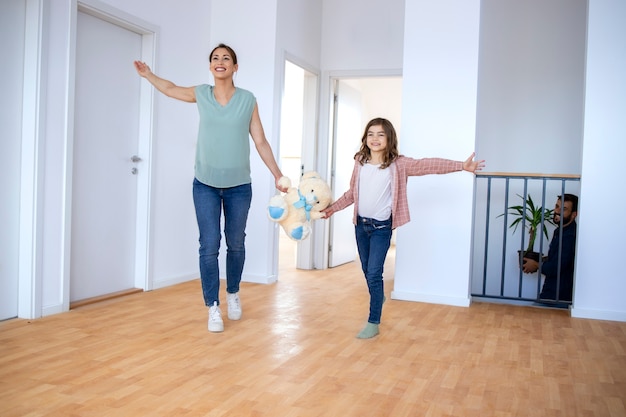 Feliz mãe e filha segurando o ursinho de pelúcia e sentindo-se animadas enquanto se mudava para a nova casa.