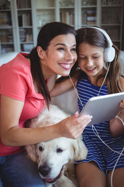 Feliz mãe e filha sentada com cachorro e ouvindo música em fones de ouvido