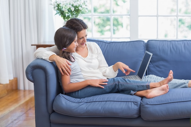 Feliz mãe e filha sentada no sofá e usando o laptop