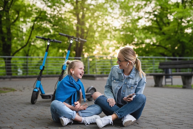 Feliz mãe e filha sentadas em uma estrada após um passeio de scooters elétricos no parque da cidade