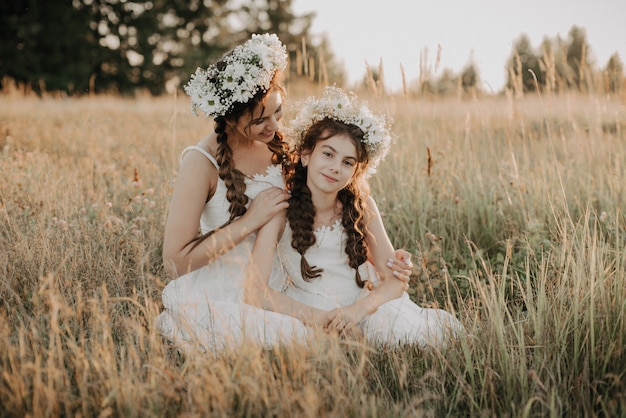 Feliz mãe e filha sorrindo e abraçando na grama no campo no verão