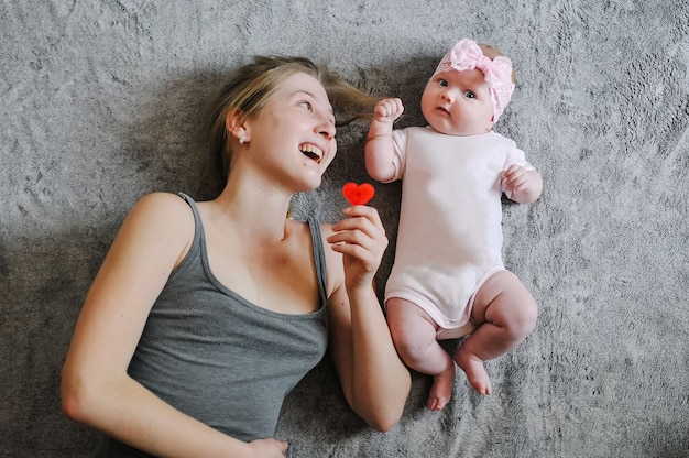 Feliz mãe e filha. Uma garotinha, o bebê, recém-nascido, mãe está deitada na cama de superfície, brincando com brinquedos. Sessão de fotos 4-5 meses. colocação plana. vista do topo.