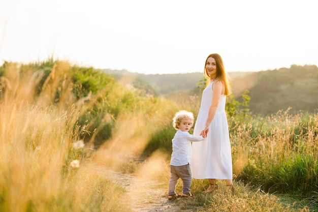 Feliz mãe e filho estão andando em campo pitoresco ao pôr do sol