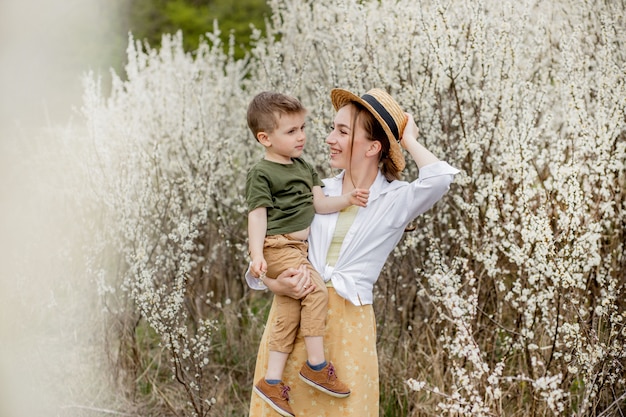 Feliz mãe e filho se divertindo juntos. Mãe suavemente abraça o filho. No fundo as flores brancas florescem. Dia das Mães