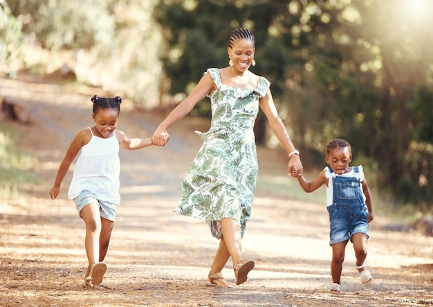 Feliz mãe e filhos andando em uma floresta de mãos dadas na natureza em alegre felicidade e sorrindo Família negra de uma mãe e suas filhas se unindo em uma caminhada divertida no ambiente natural ao ar livre