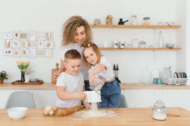 Feliz mãe e filhos misturando ingredientes para bolo caseiro, torta ou massa de biscoito na cozinha.