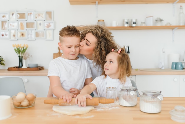 Feliz mãe e filhos misturando ingredientes para bolo caseiro, torta ou massa de biscoito na cozinha.