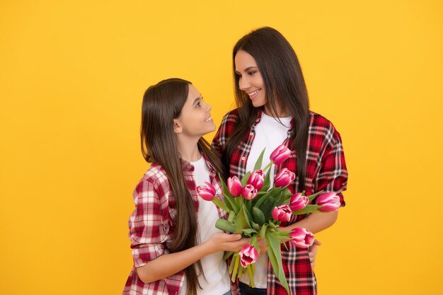 Feliz mãe e menina com flores de tulipa em fundo amarelo