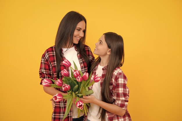 Feliz mãe e menina com flores de tulipa em fundo amarelo