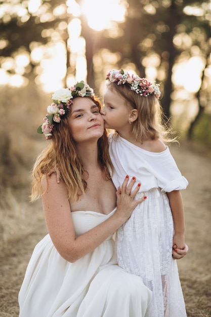 Feliz mãe elegante e sua linda filha com grinaldas de flores em um parque ao pôr do sol