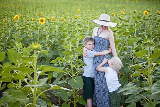 Feliz mãe grávida abraçando dois filhos pequenos em um campo de girassóis florescendo