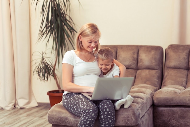 Feliz mãe grávida com seu filho filho usando o laptop em casa na sala de estar