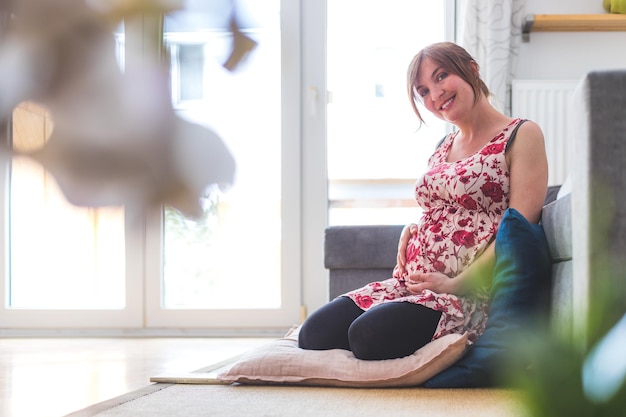 Feliz mãe grávida está sentada no chão abraçando sua barriga