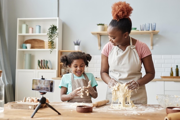 Feliz mãe negra e filha assando juntas na cozinha de casa