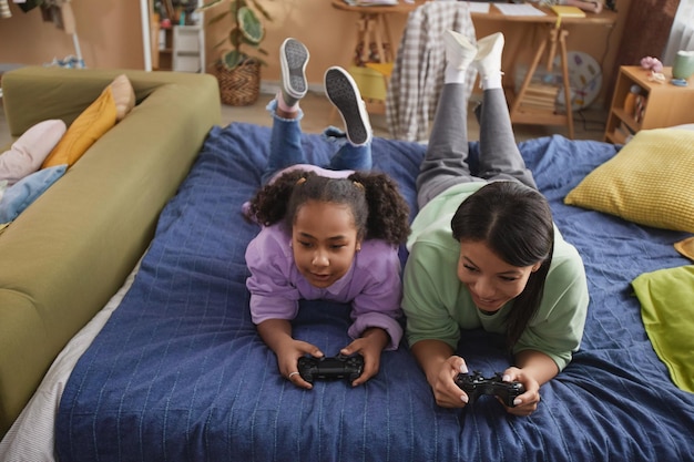 Feliz mãe negra e filha jogando videogame deitada na cama em casa