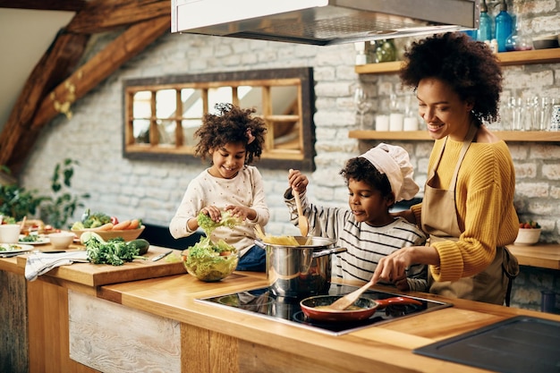 Feliz mãe negra e seus filhos preparando comida na cozinha