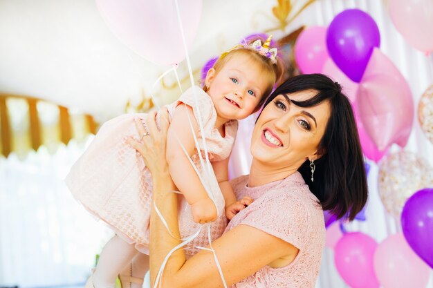 Feliz mãe segura a filha nas mãos no fundo de muitas bolas infláveis