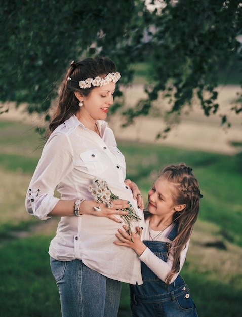 Feliz mamá embarazada con su pequeña hija a pasear en un día de verano.