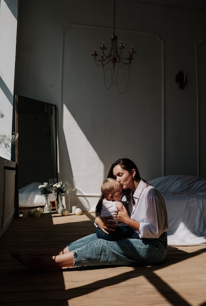 Feliz mamá morena y niña besándose en el piso de madera en los rayos de luz