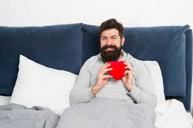 Feliz mañana Hipster barbudo necesita amor Falta de amor Hombre descansando en la cama Buscando pareja Cuida el corazón Amor y relaciones Día de San Valentín Regalo sorpresa Celebración navideña