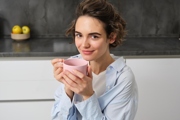 Feliz mañana retrato de feliz mujer morena bebe una taza de café en su cocina y sonriendo acogedor