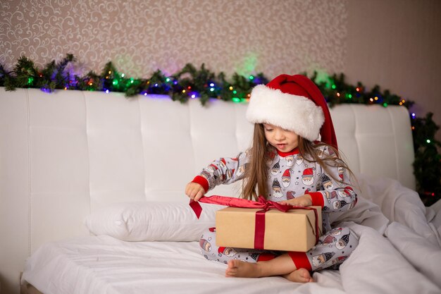 Feliz Manhã de Natal Uma garota alegre e divertida de pijama e boné de Papai Noel com uma caixa de presente