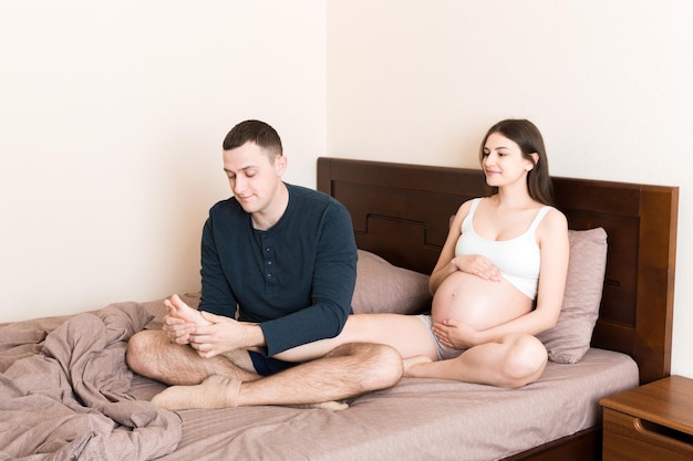 Feliz marido de familia embarazada masajeando las piernas de su esposa embarazada y sentados juntos en el sofá