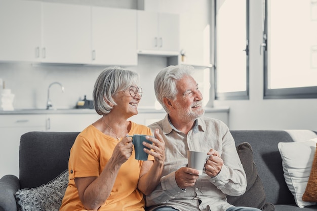 Feliz marido y mujer maduros de los años 50 se sientan a descansar en un cómodo sofá en la sala de estar disfrutan del té hablando sonriente pareja de ancianos de los años 60 relajarse en el sofá en casa beber café charlar hablar reír en el fin de semana de ocioxA