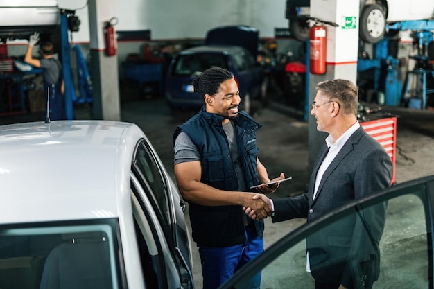 Feliz mecânico de automóveis afro-americano apertando as mãos de um cliente na oficina de reparação de automóveis