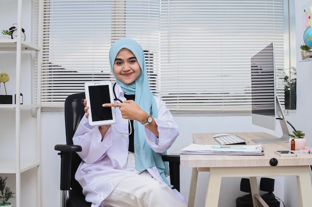 Feliz médica muçulmana em hijab mostrando tablet digital com tela em branco, maquete, cópia spa