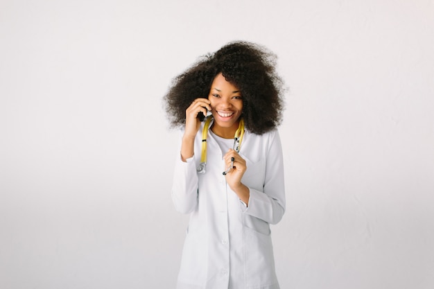 Feliz médico africano interno médico no estúdio com um estetoscópio no hospital em fundo branco e falando ao telefone