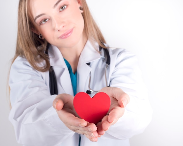 Feliz médico feminino com coração vermelho, na parede branca