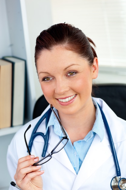 Feliz médico feminino segurando óculos sorrindo para a câmera