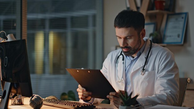Feliz médico leyendo registros en el hospital nocturno primer plano médico alegre revisando