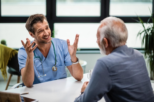 Feliz médico masculino comunicándose con un anciano durante una cita médica en su oficina