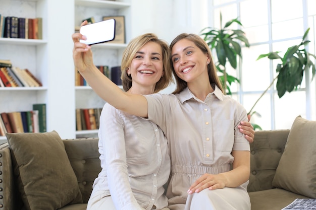 Feliz meia-idade mãe e filha tomando selfie em casa.