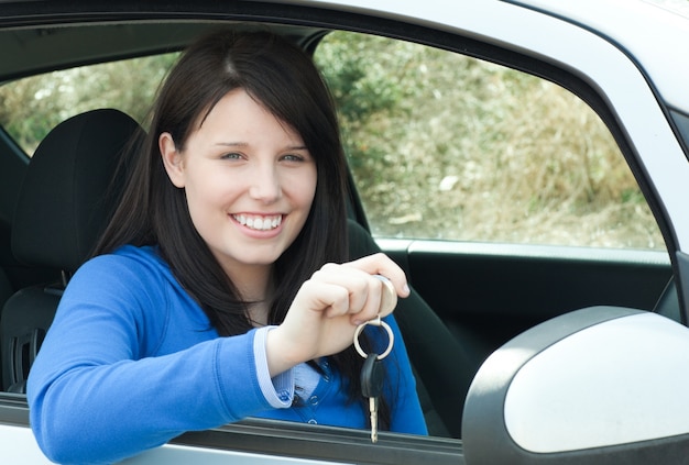 Feliz menina adolescente sentada em seu carro segurando chaves