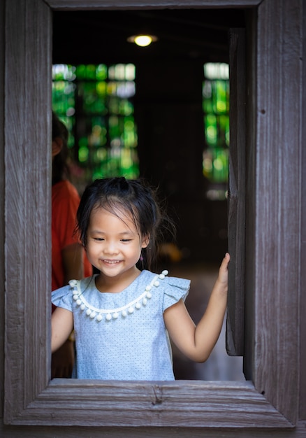 Feliz menina asiática em pé junto à janela